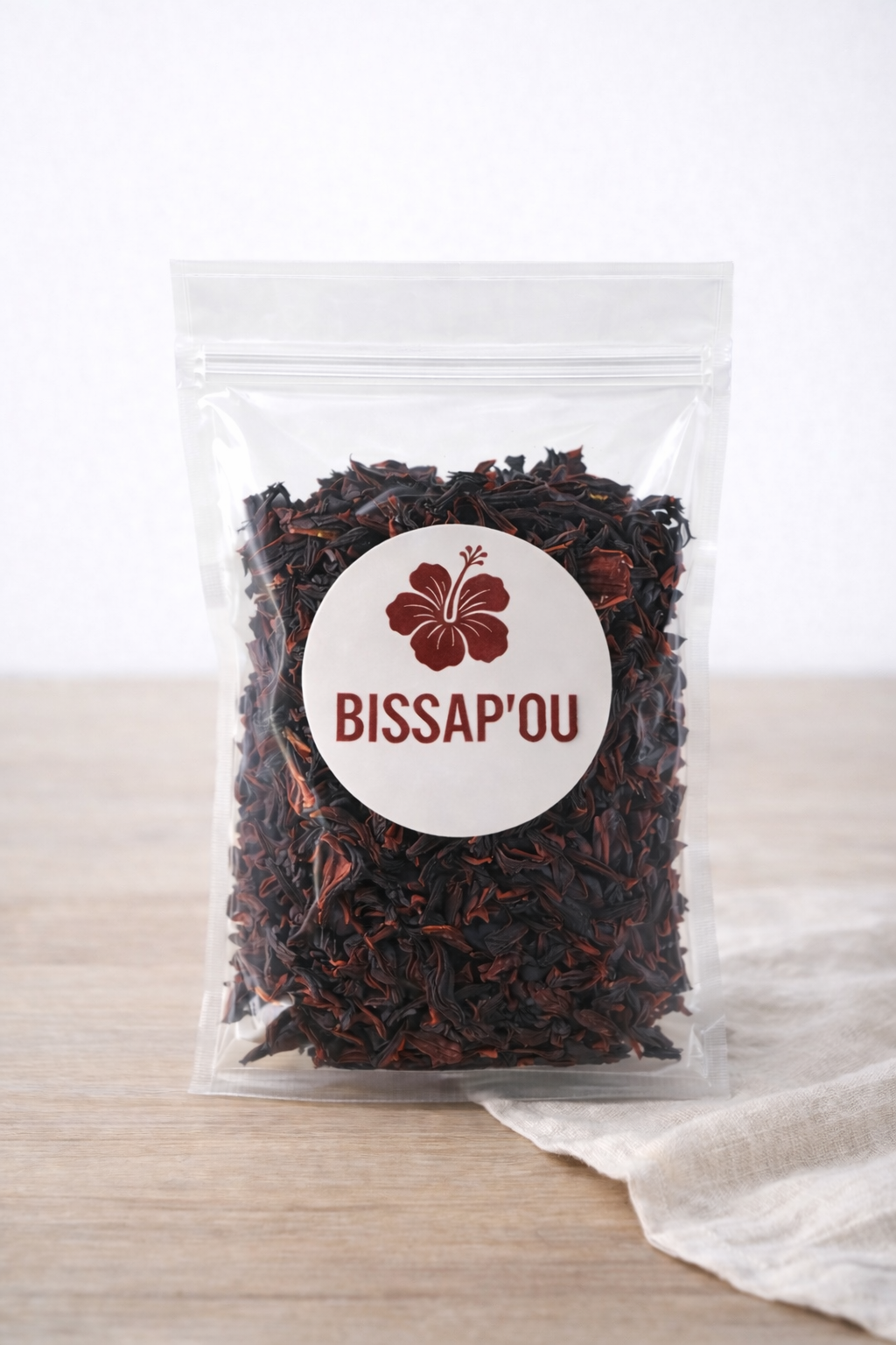 Sachet transparent de bissap séché posé sur une table en bois, avec une étiquette BISSAP’OU.