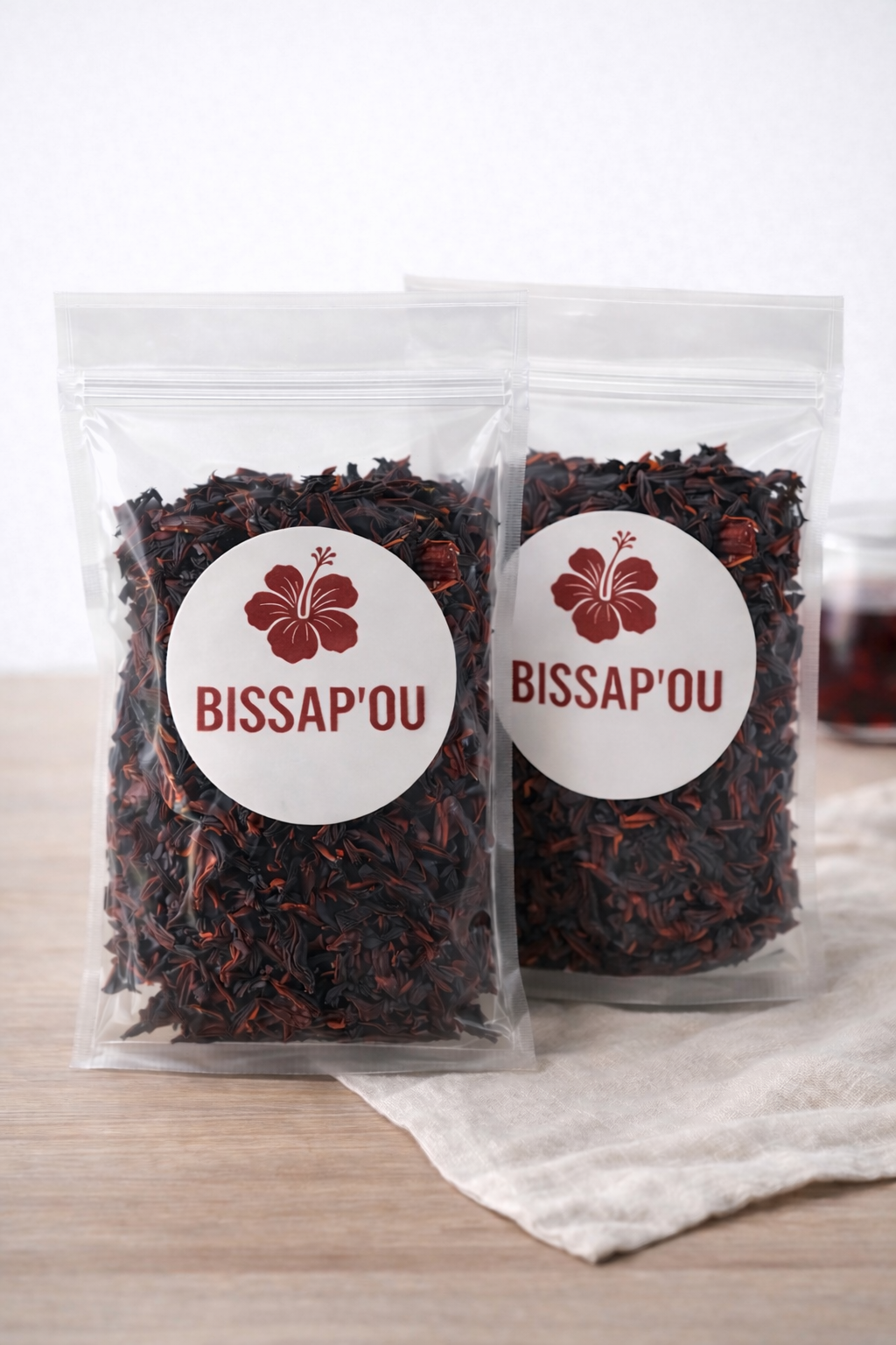 Deux sachets de bissap séché présentés sur une table en bois, à côté d’un tissu clair.